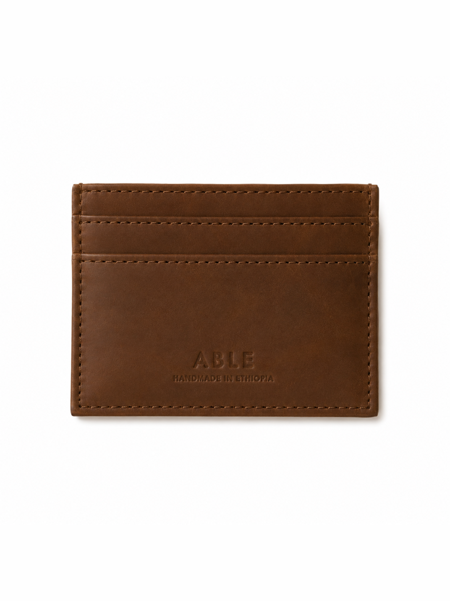 A brown leather card holder wallet with visible stitching and debossed 'ABLE' branding on the front, shown against a plain white background. #Color_Whiskey