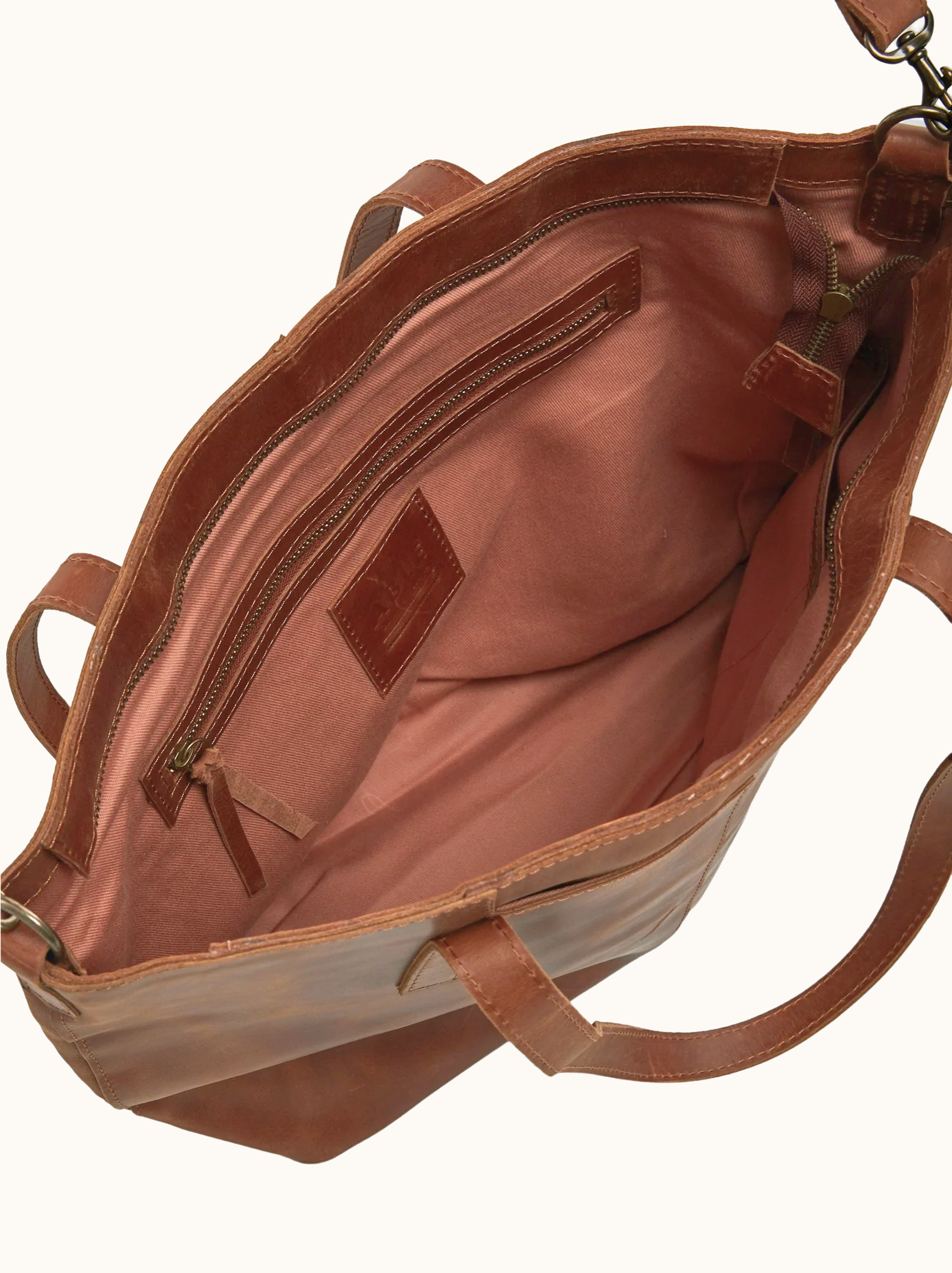 Lined interior of brown leather bag with zipper pocket and a strap on a white background #Color_Whiskey
