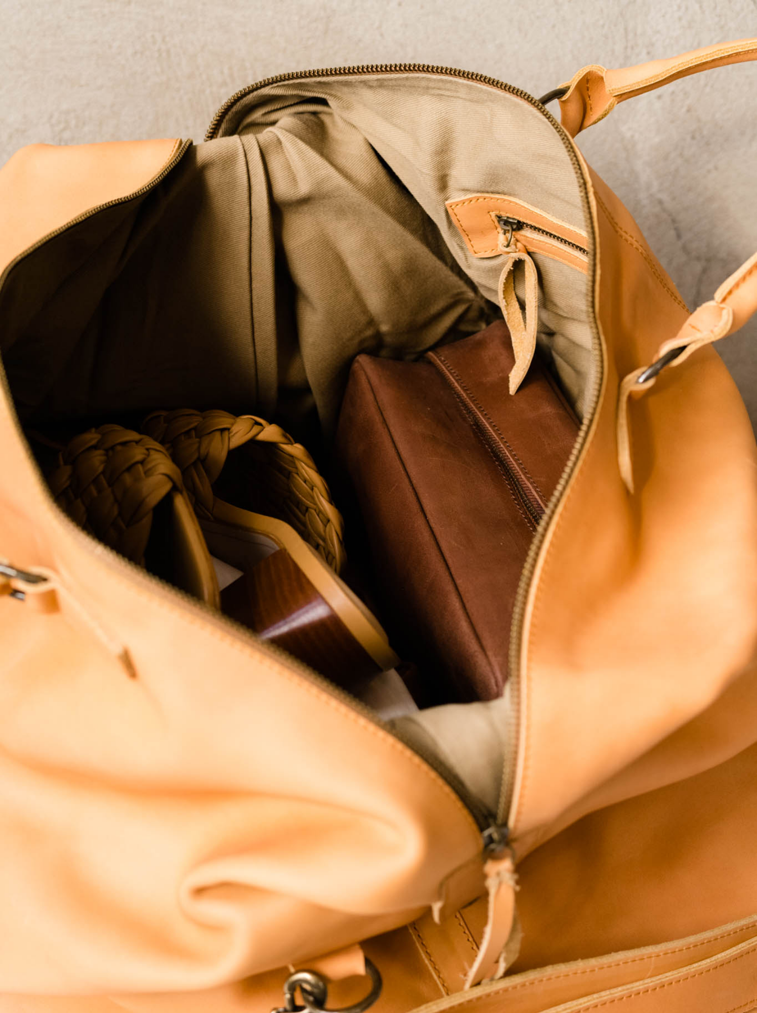 Close up of the interior of the cognac weekender with interior zipper pocket, a dopp kit and shoes. #Color_Cognac