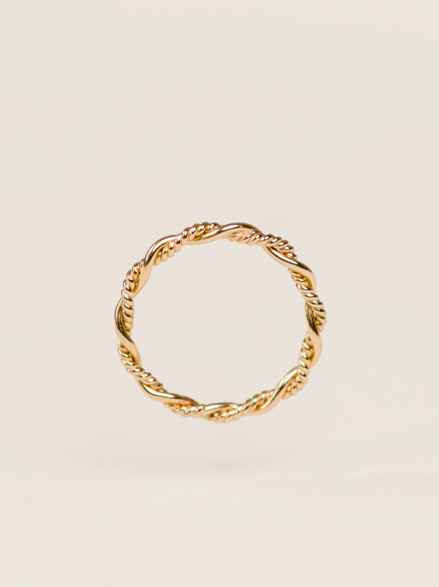 Floating gold braided ring on a neutral background.