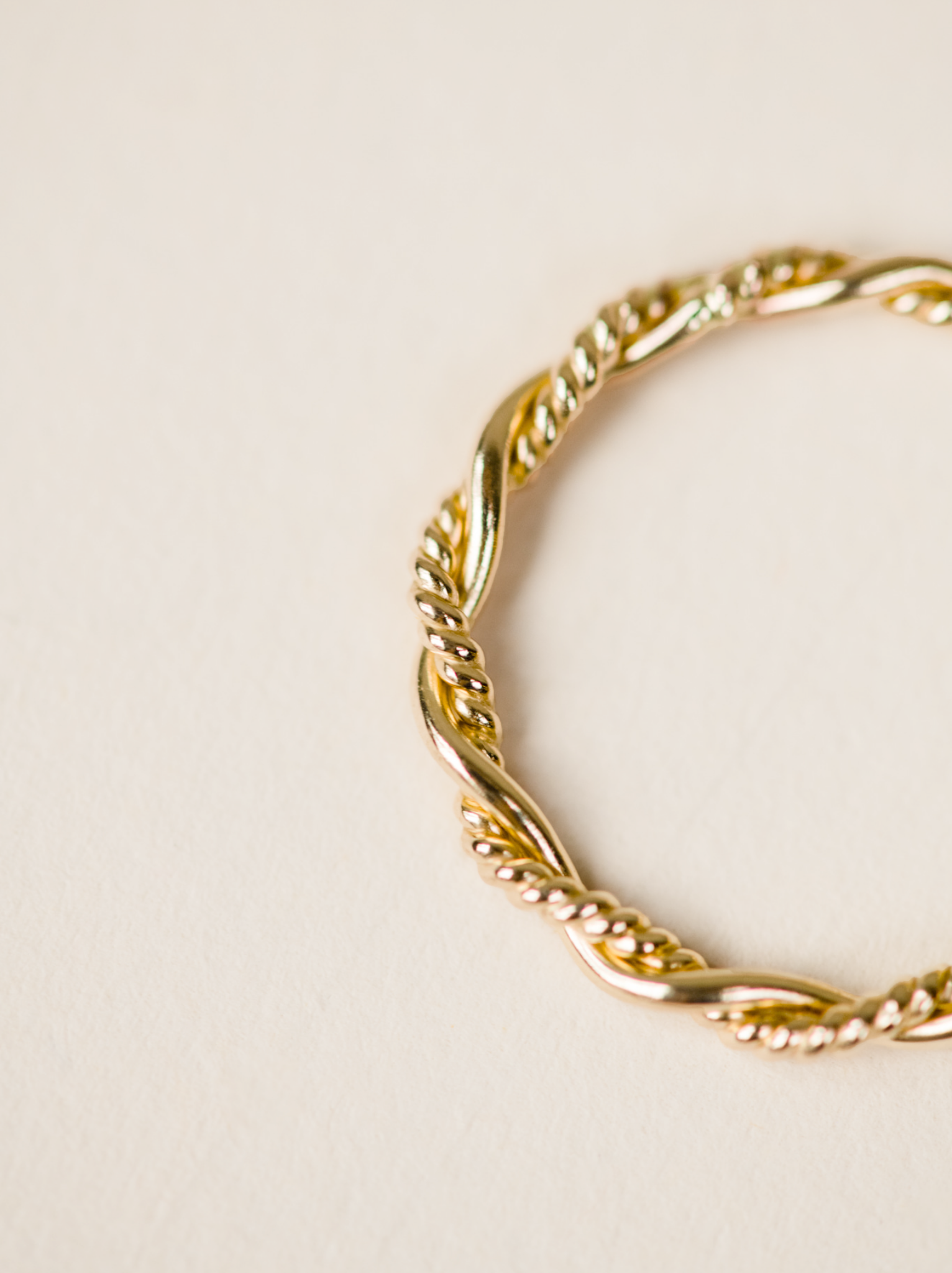 Close up of braided detail of gold ring on neutral background.