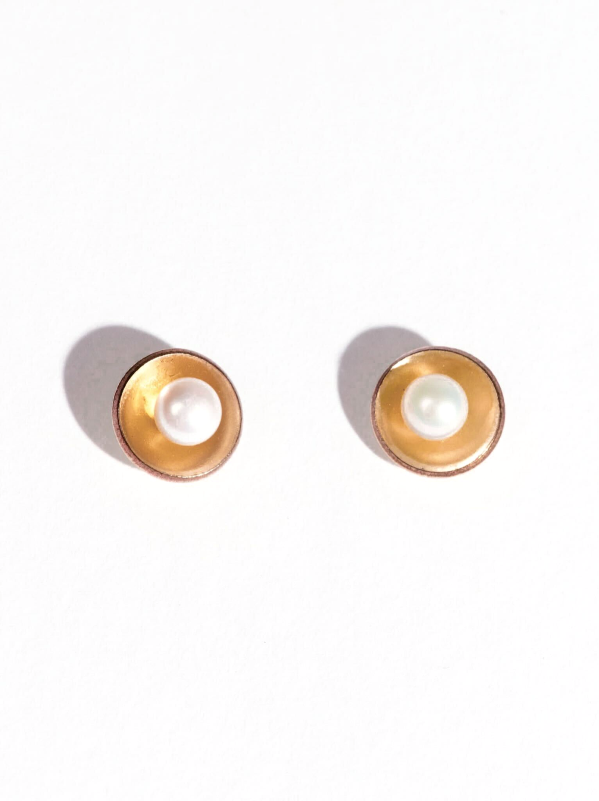 Pair of gold earrings with a pearl center on a white background