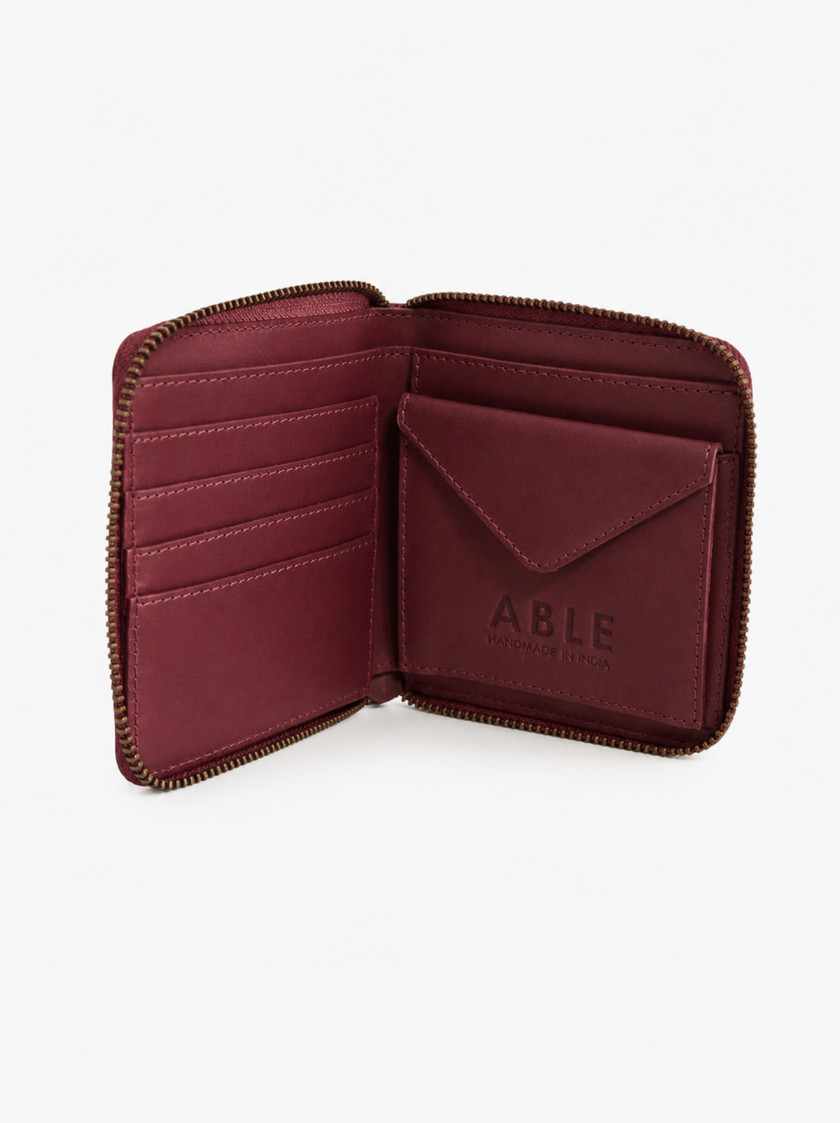 An open burgundy zip-around wallet with multiple card slots and an envelope-style card pocket, shown on a clean white background. The brand name 'ABLE' is embossed on the card pocket. #Color_Oxblood
