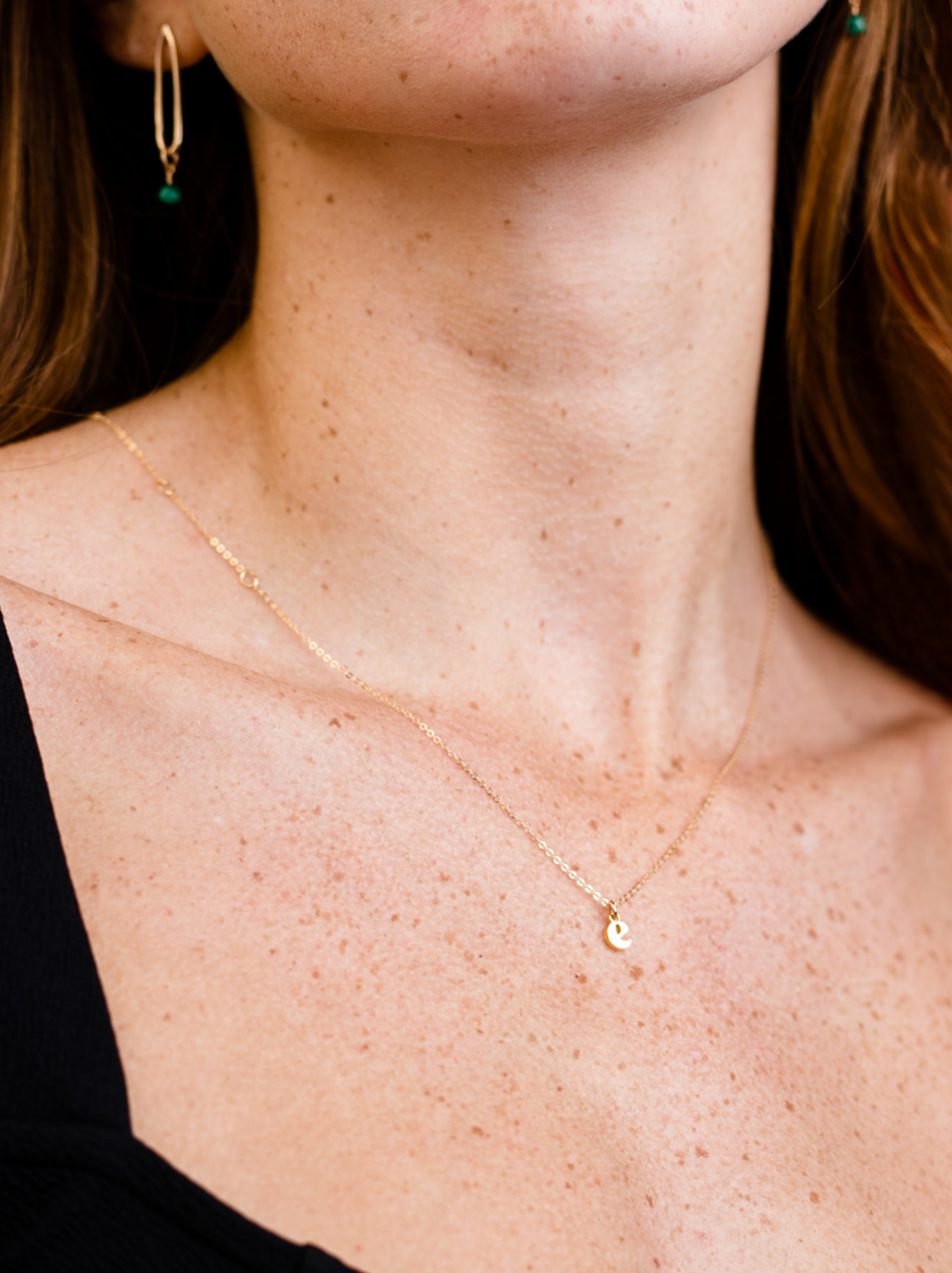 Woman wearing a lowercase letter "e" pendant necklace.