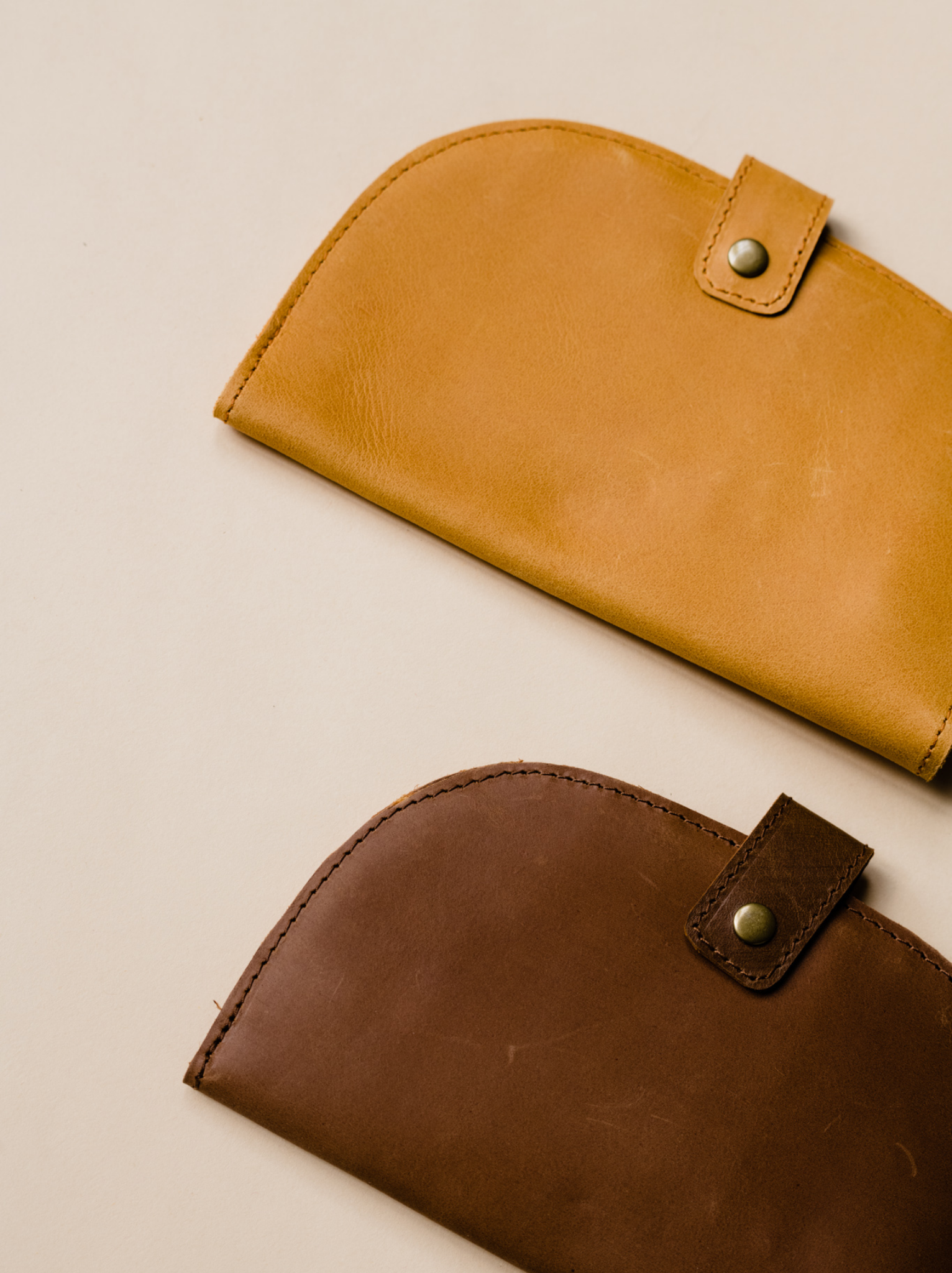 Cognac and Whiskey bifold wallets on solid background with snap close features.