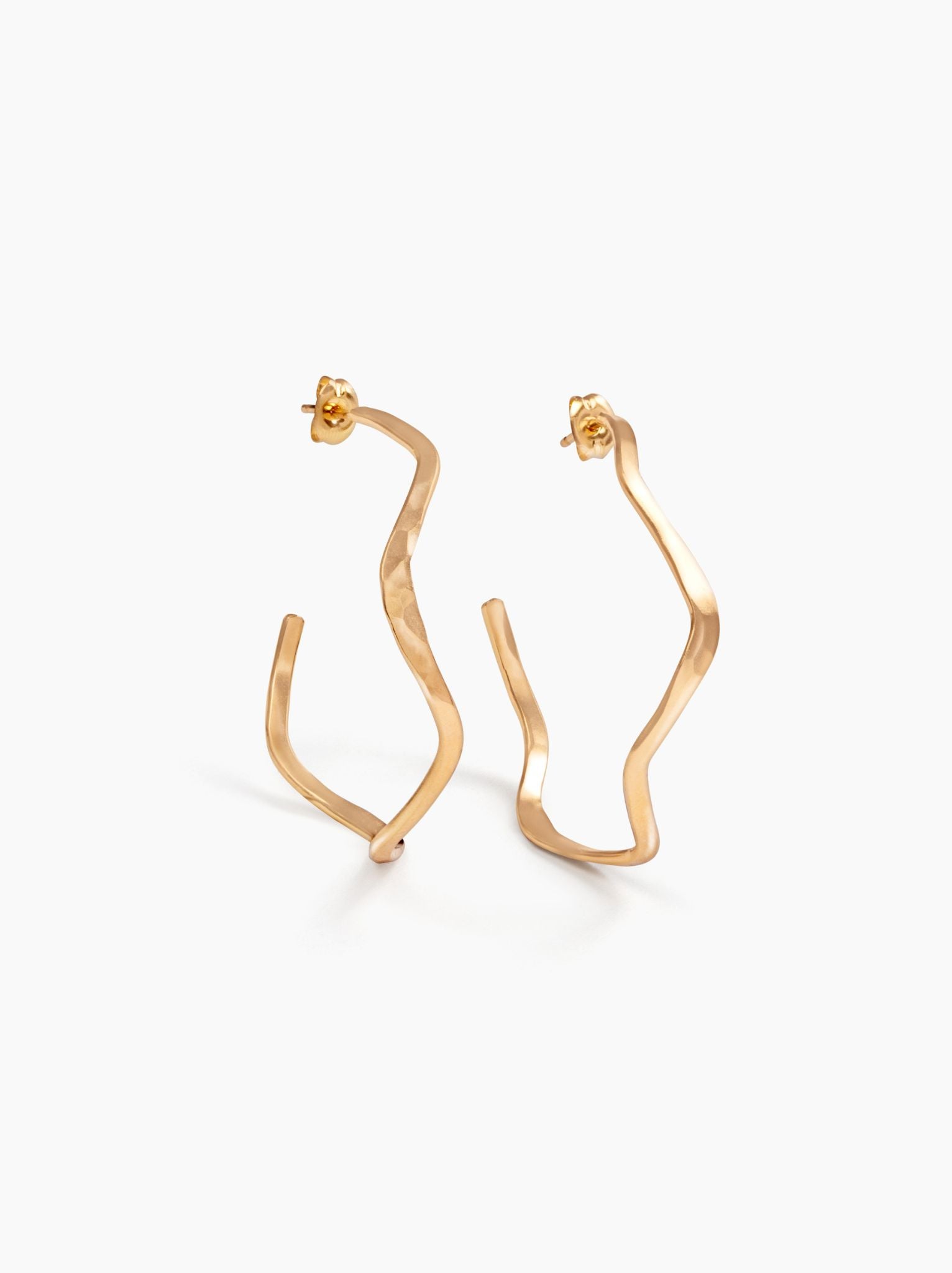Angled view of gold wavy hoop earrings with ear posts on a white background.