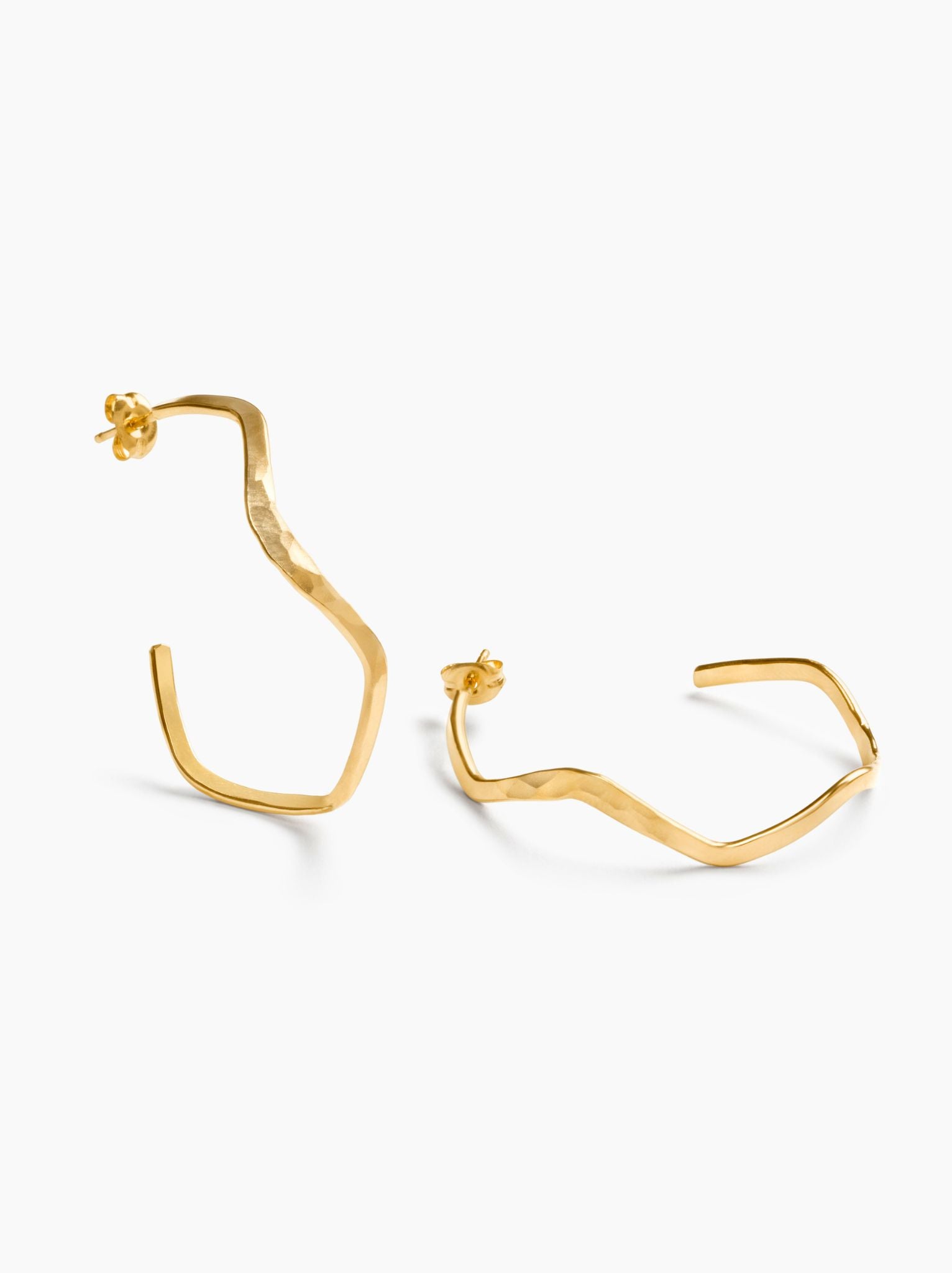 Gold wavy hoop earrings with one up and one lying down on a white background.