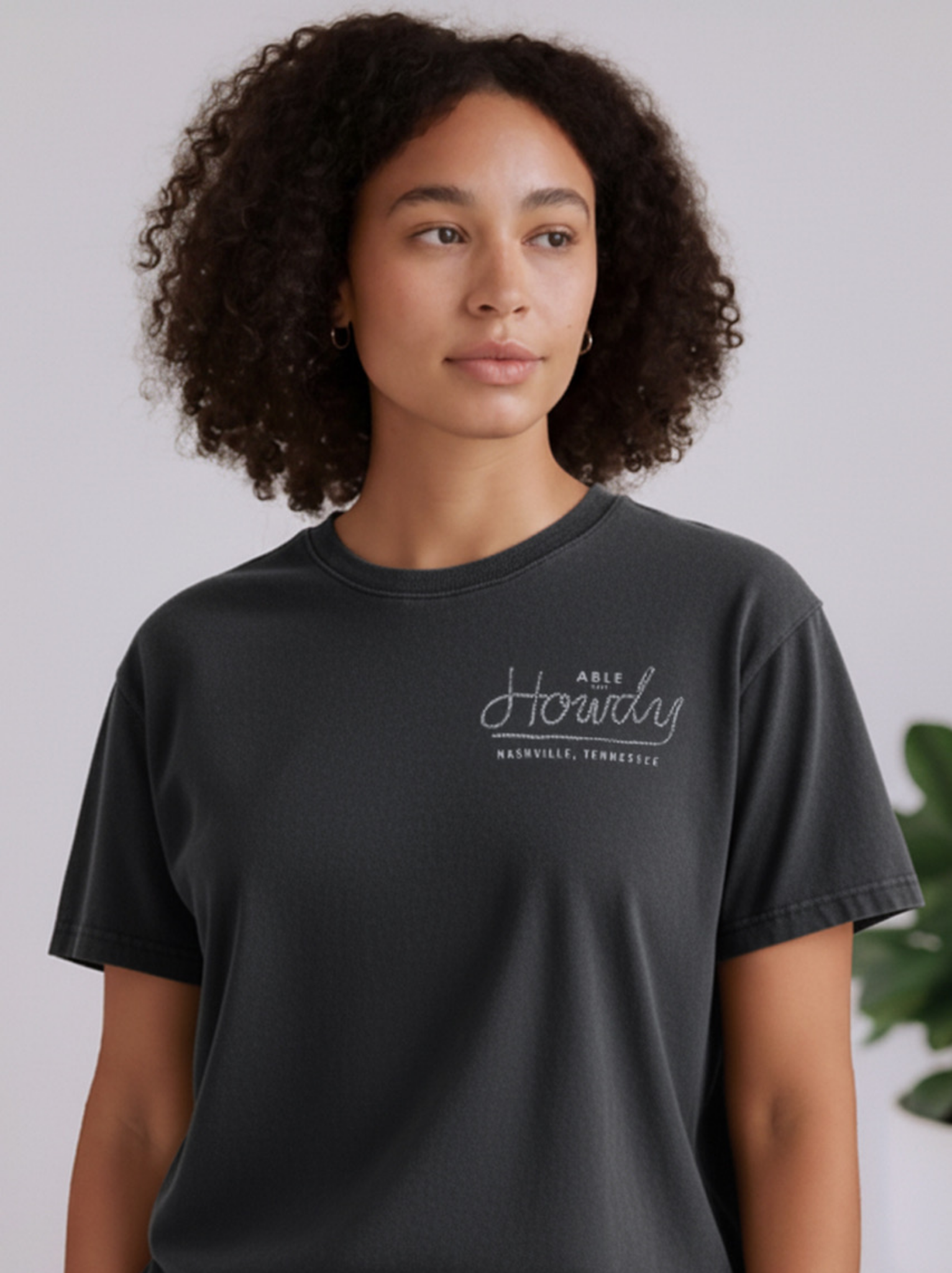 Person wearing a black t-shirt Say Hi Tee with 'Howdy Nashville, Tennessee' text on a plain background