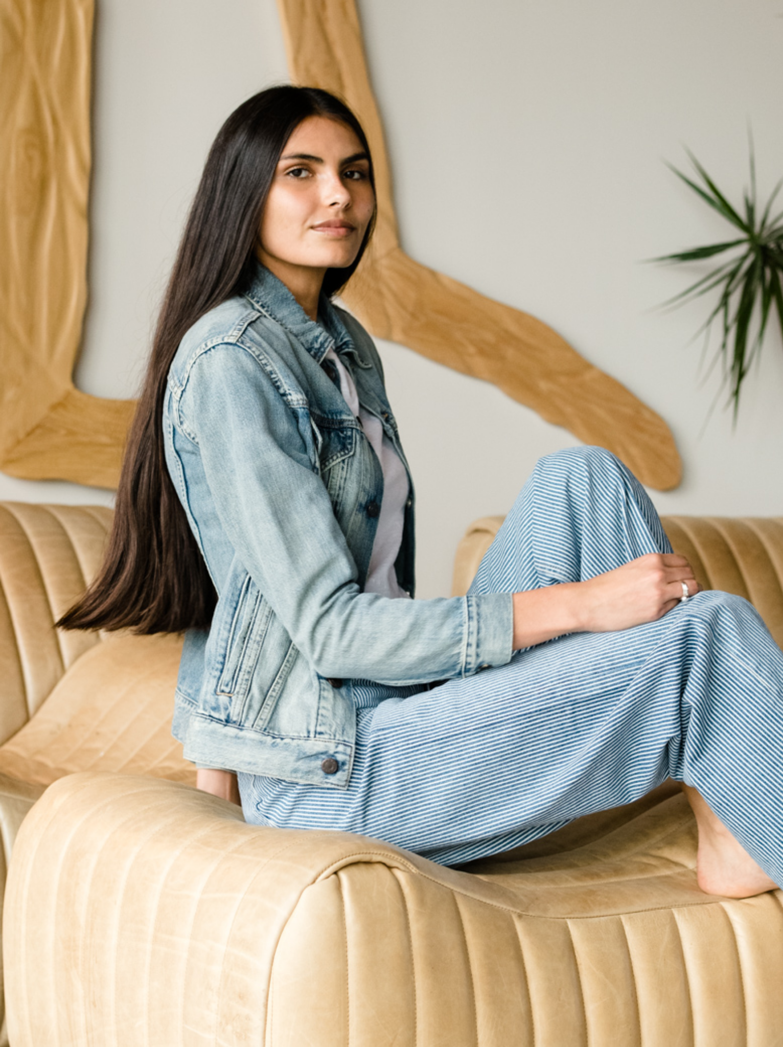 Woman wearing The Merly Jacket sitting on a beige couch.