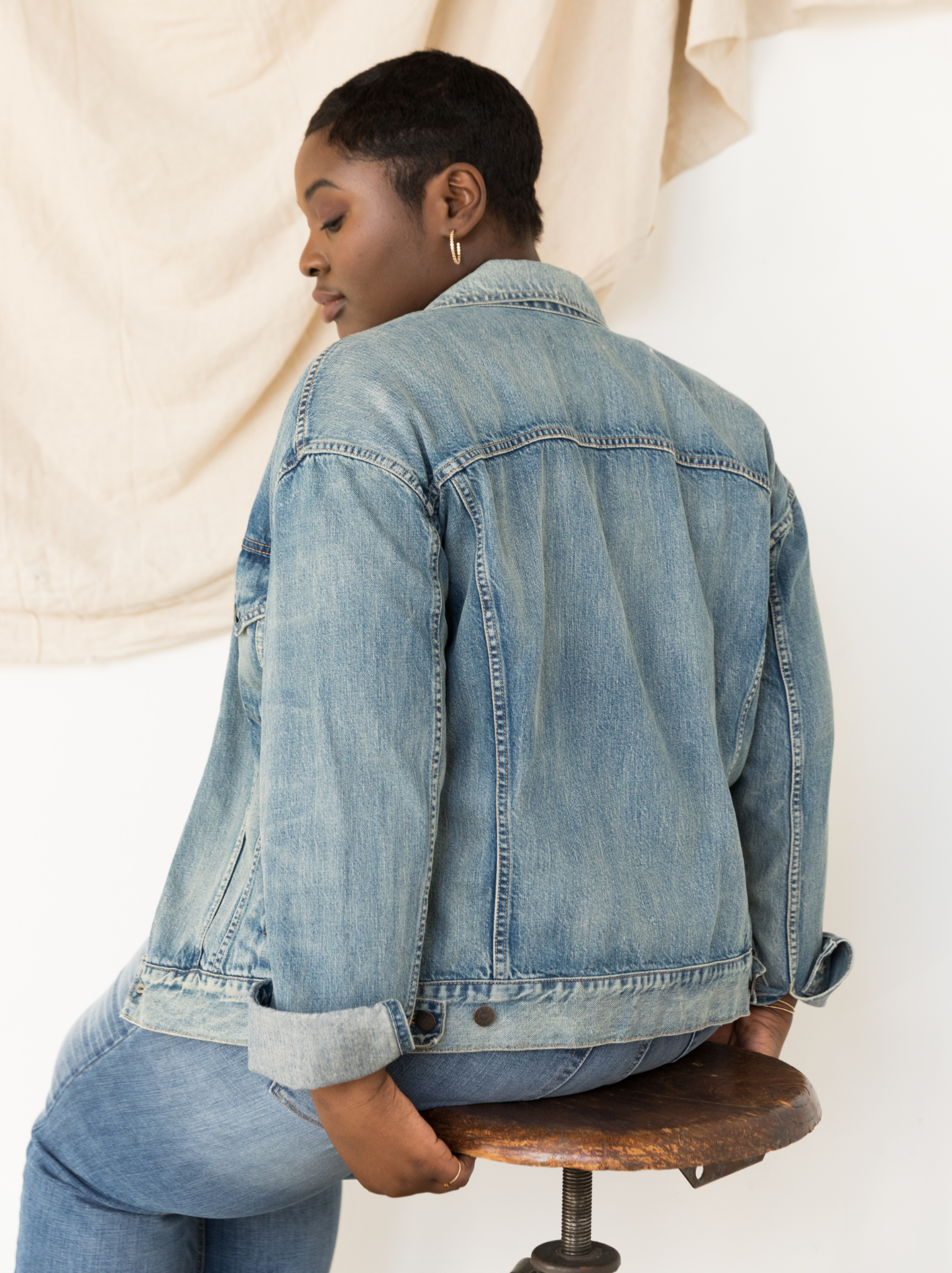 Person wearing The Merly Jacket sitting on a wooden stool against a neutral background