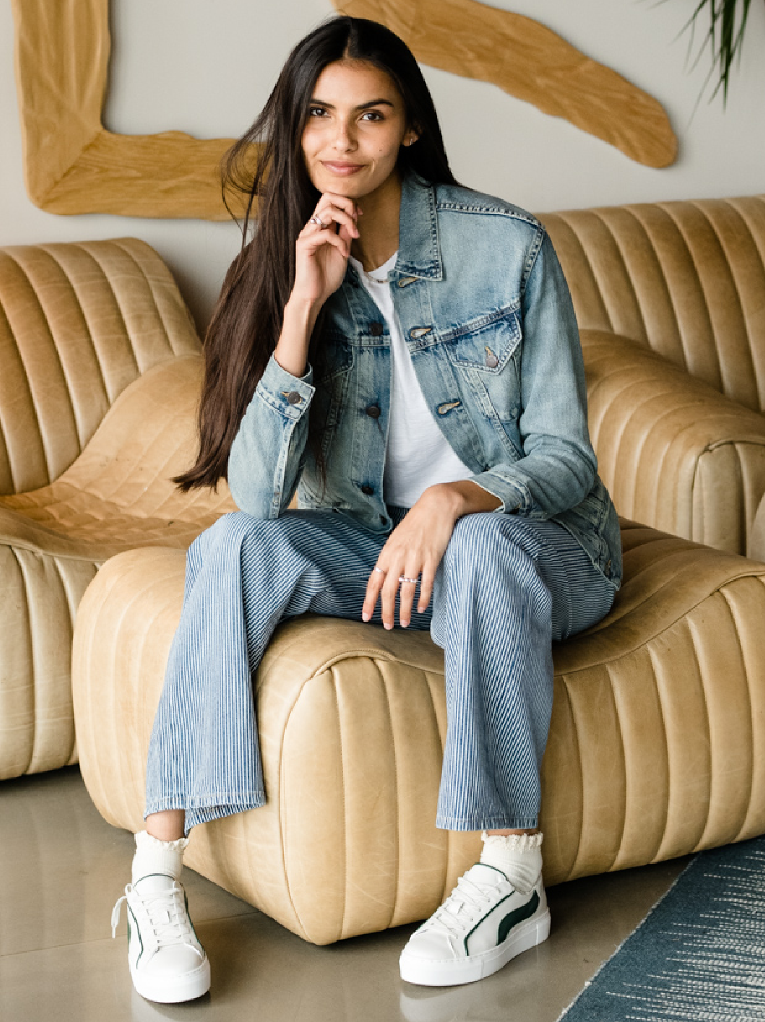 Woman sitting on a beige couch wearing The Merly Jacket and jeans.
