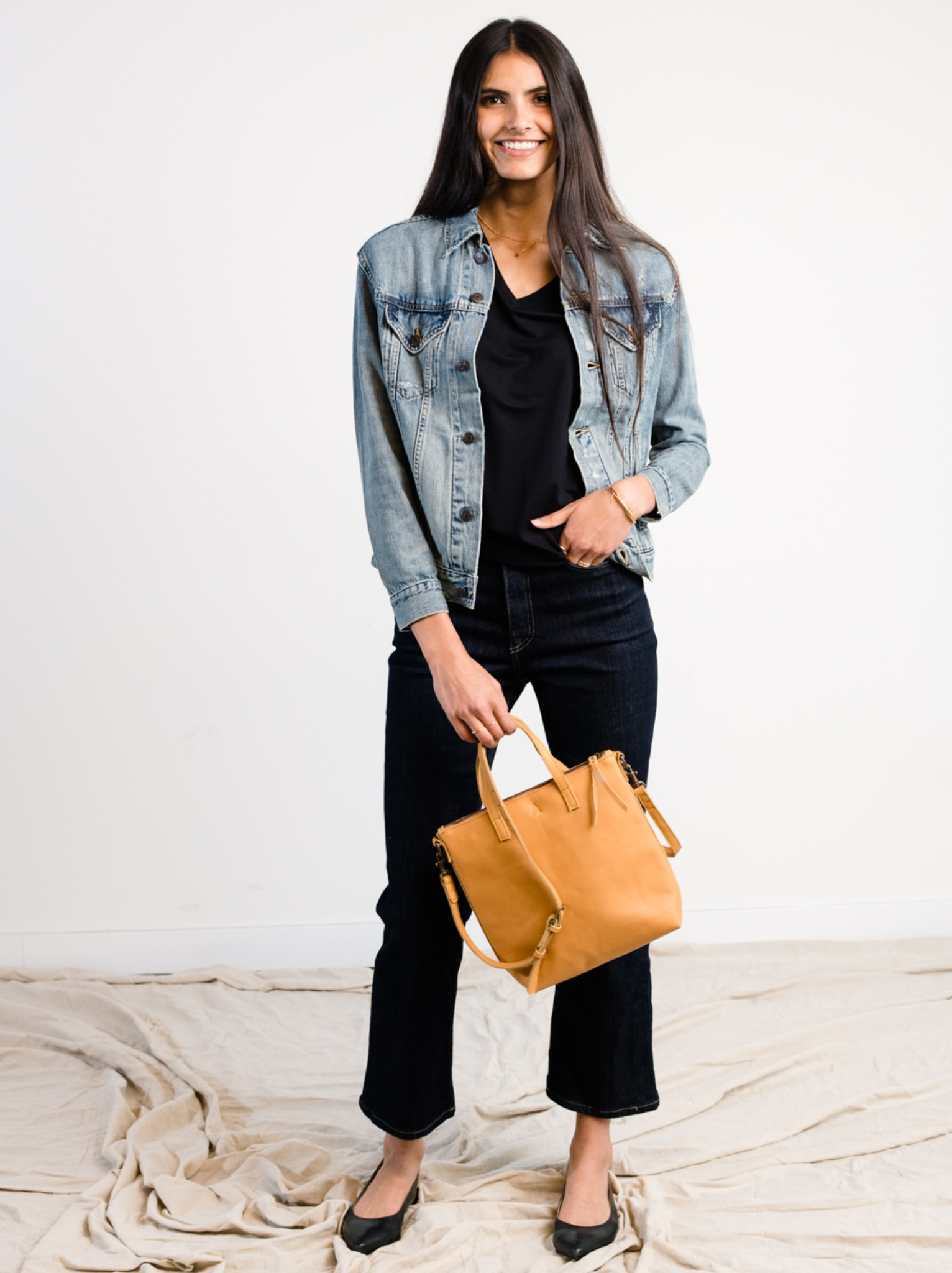 Woman wearing The Merly Jacket and holding a brown leather bag against a white background