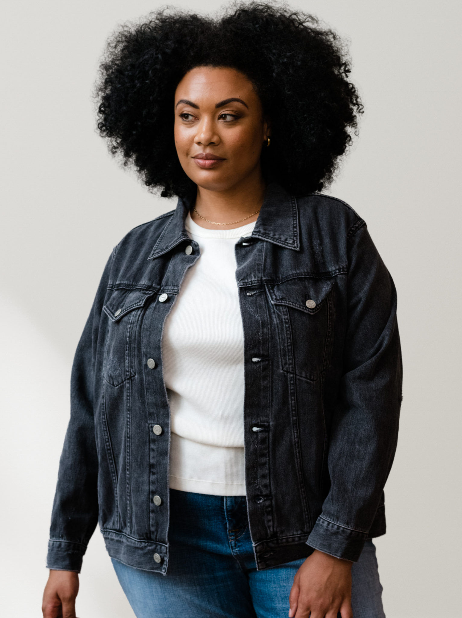 Woman wearing The Merly Jacket Washed Black over a white shirt and blue jeans on a plain background