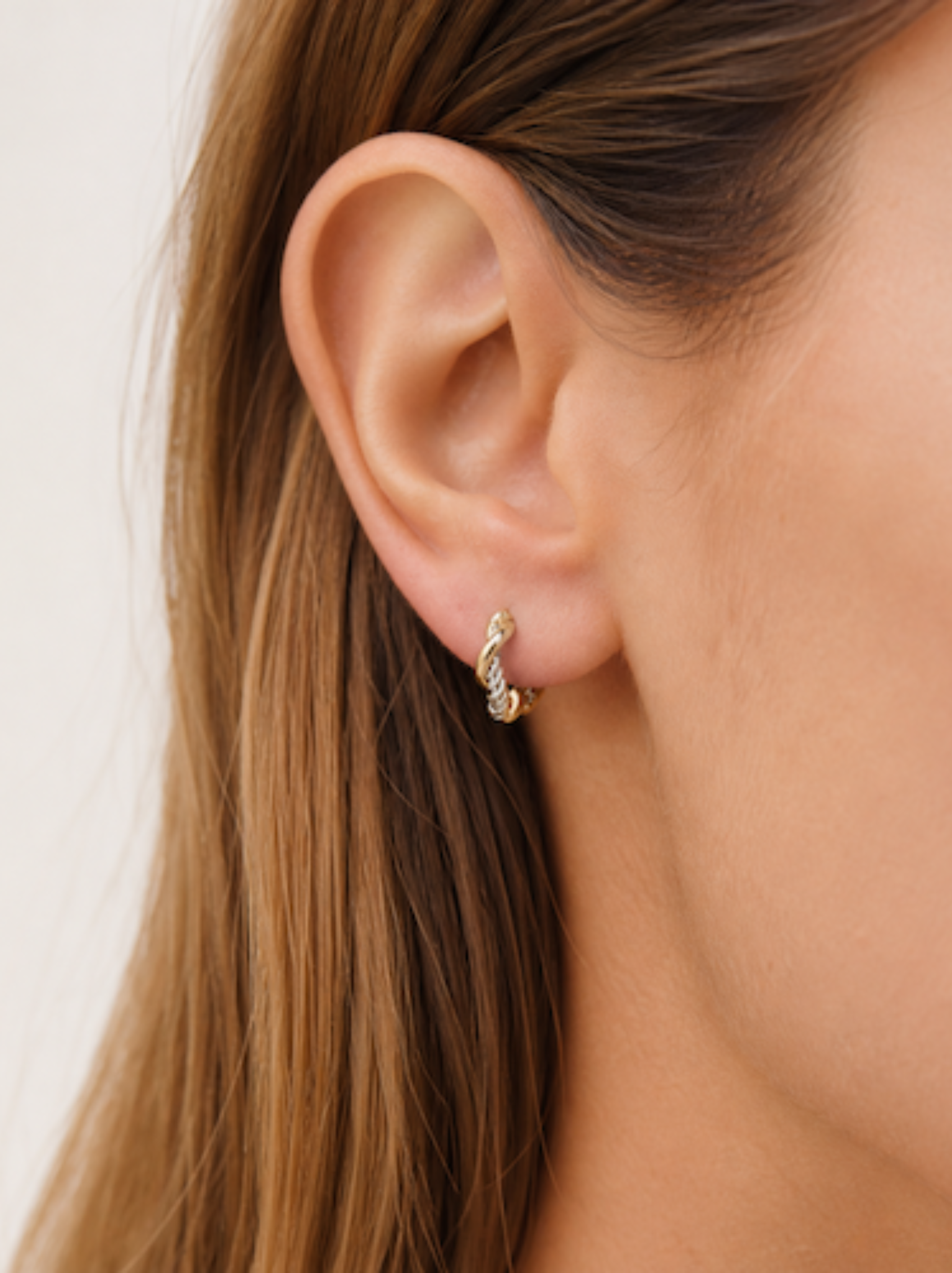 Close-up of an ear wearing a gold and silver braided mini hoop earring.