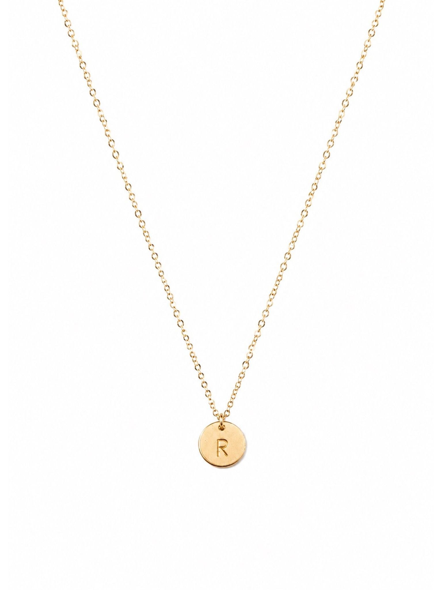 Gold necklace with a round pendant featuring the letter 'R' on a white background.