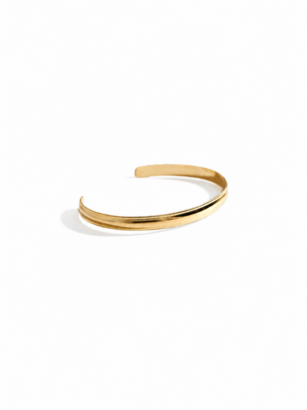 A gold-filled cuff bracelet with a smooth, flat band and textured edges on a white background.