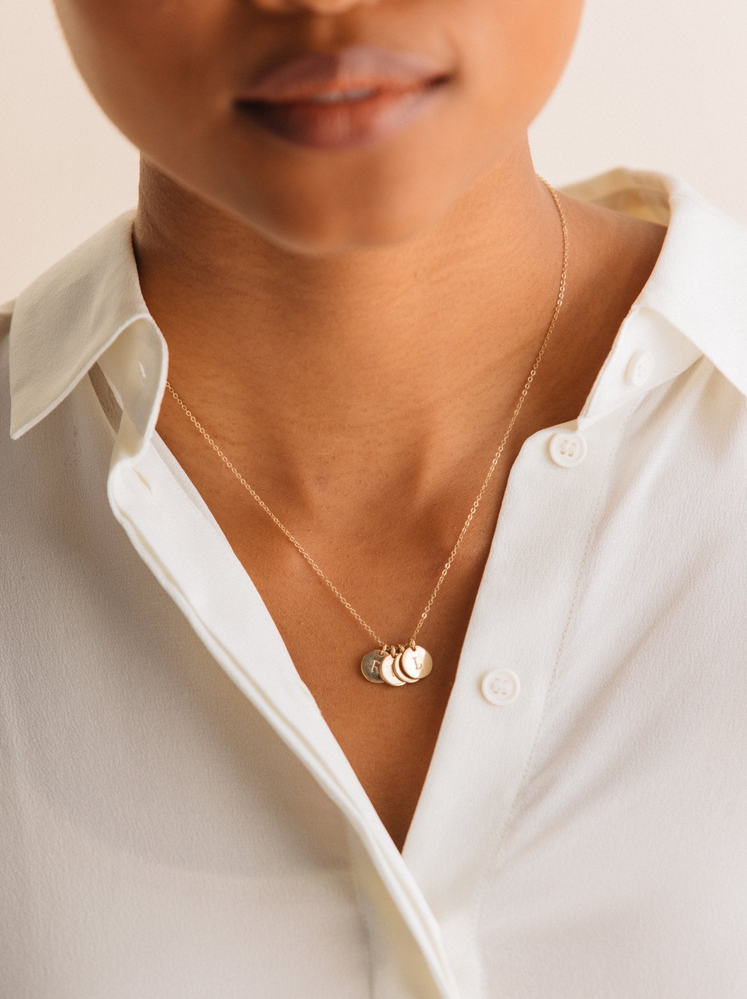 Close up of a woman wearing a gold necklace with four small pendants featuring different letters.