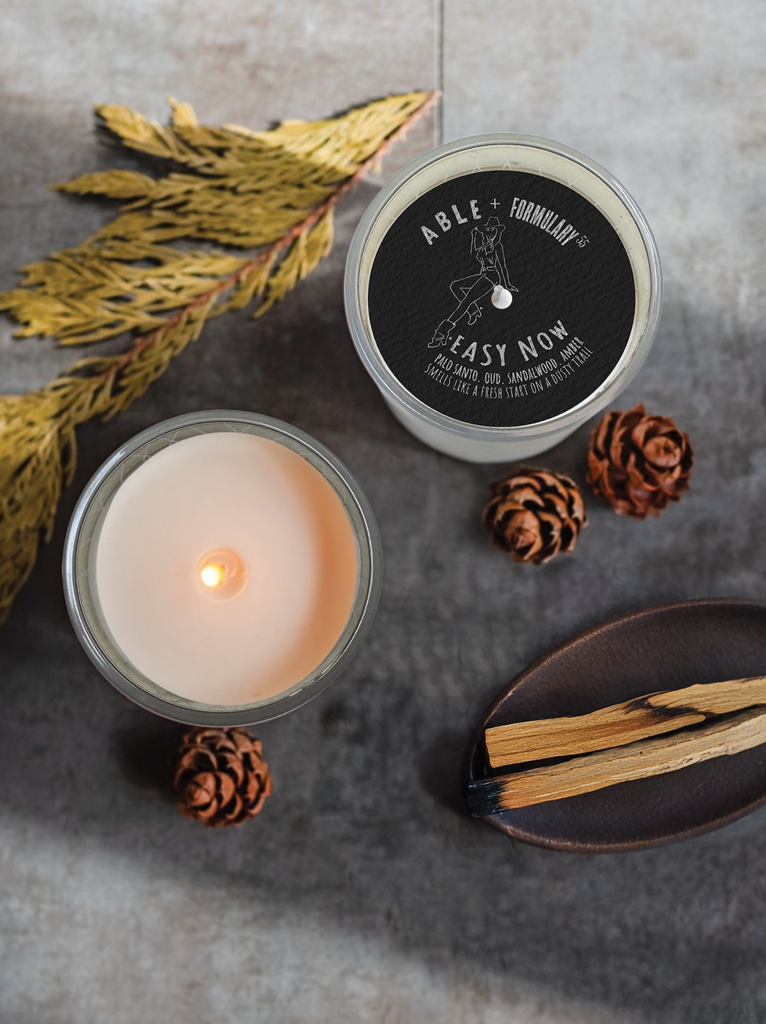 The ABLE x Formulary55 candle shown with its fragrance elements; including pieces of palo santo, peppercorns, and sandalwood.