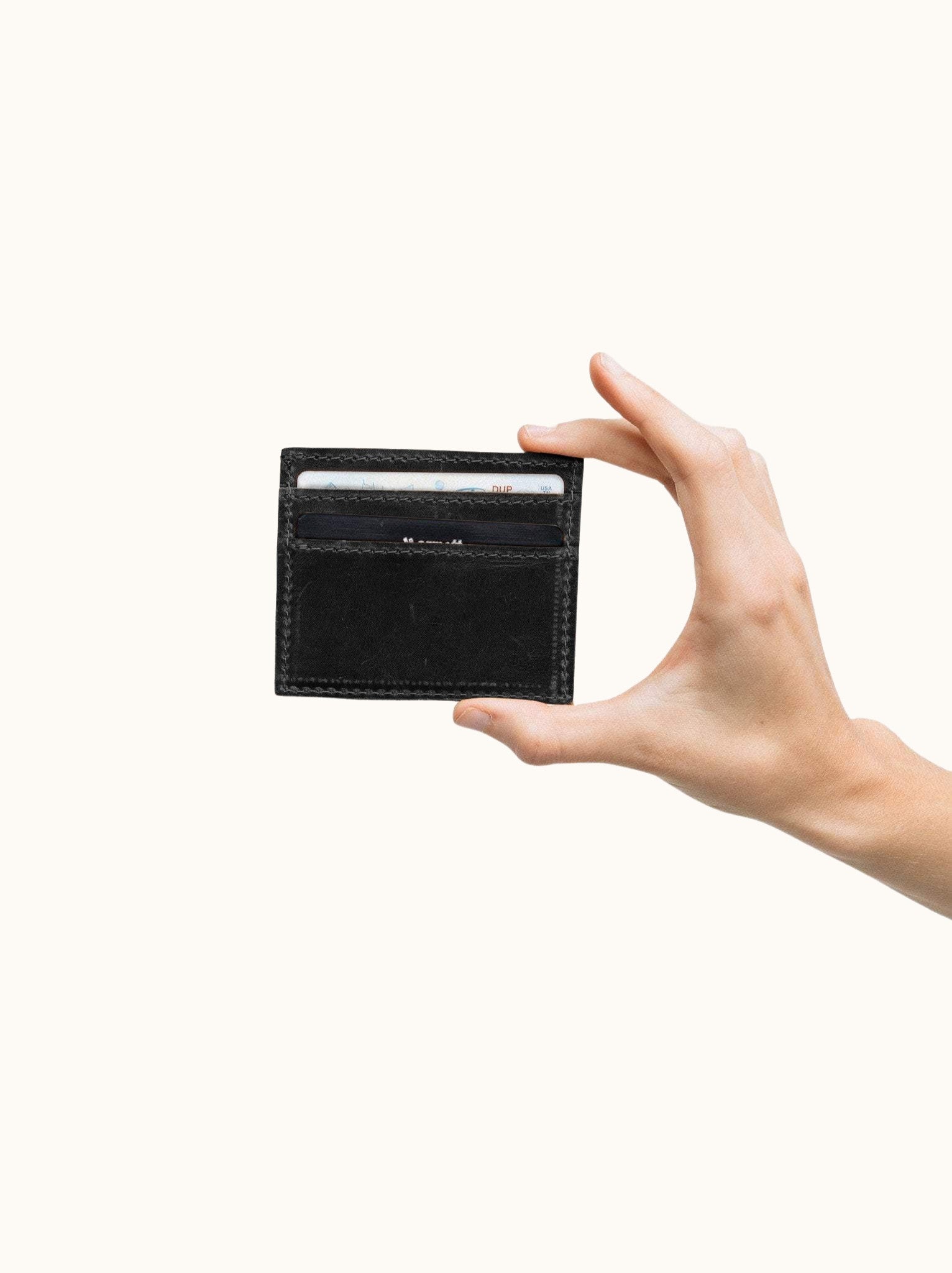 Hand holding a Alem Card Case; black leather wallet against a white background #Color_Black