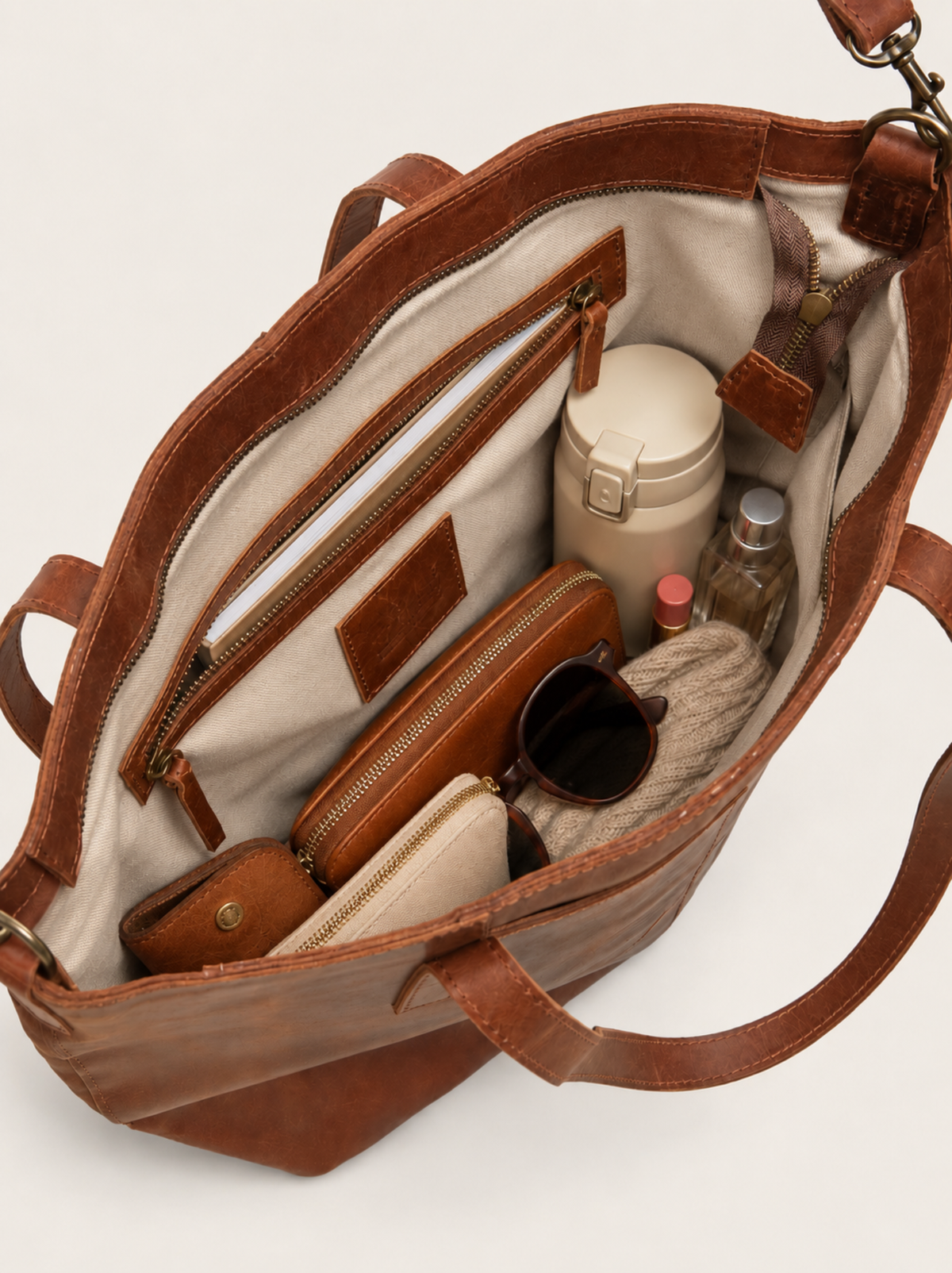 Birds eye interior shot of a whiskey tote with a water bottle, wallet, glasses, sweater and more. Tote also has an interior zipper with a notebook inside. #Color_Whiskey