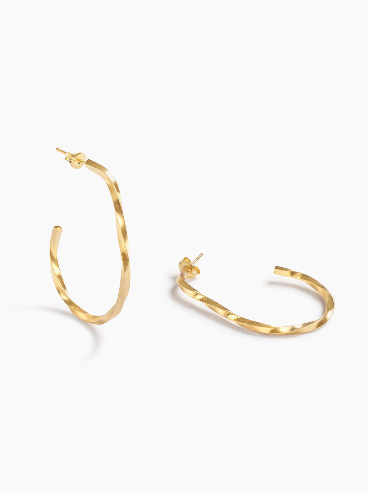 Gold hoop earrings, one standing and one lying, on a white background