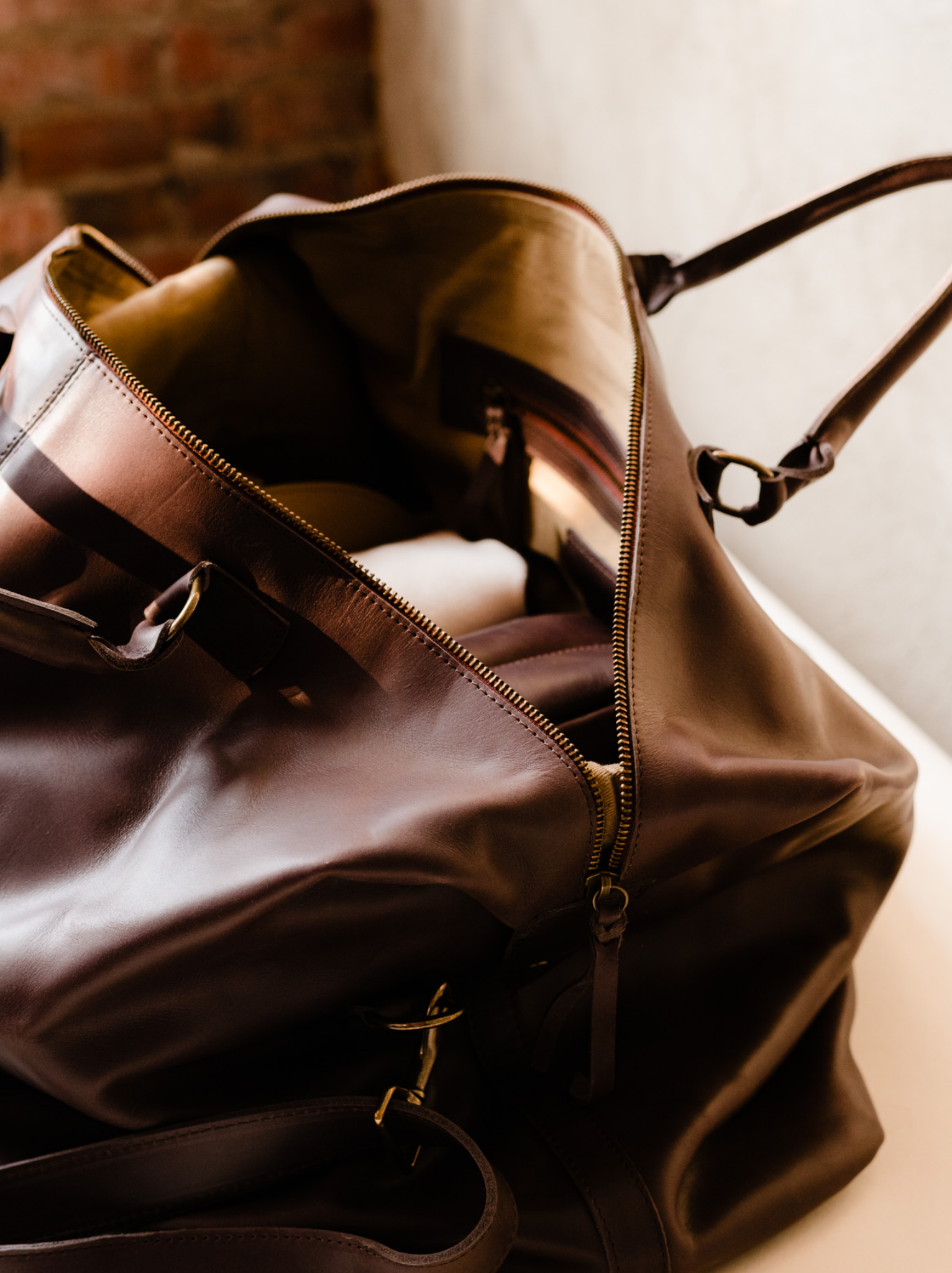 Unzipped chocolate brown leather weekender bag with interior zipper pocket and items inside. #Color_Chocolate Brown
