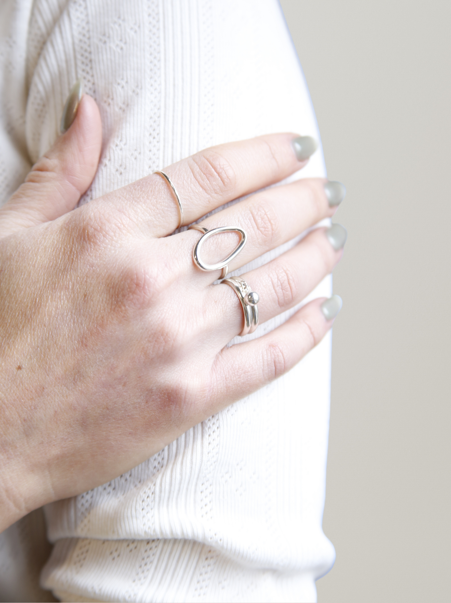 Hand wearing multiple silver rings with a plain background
