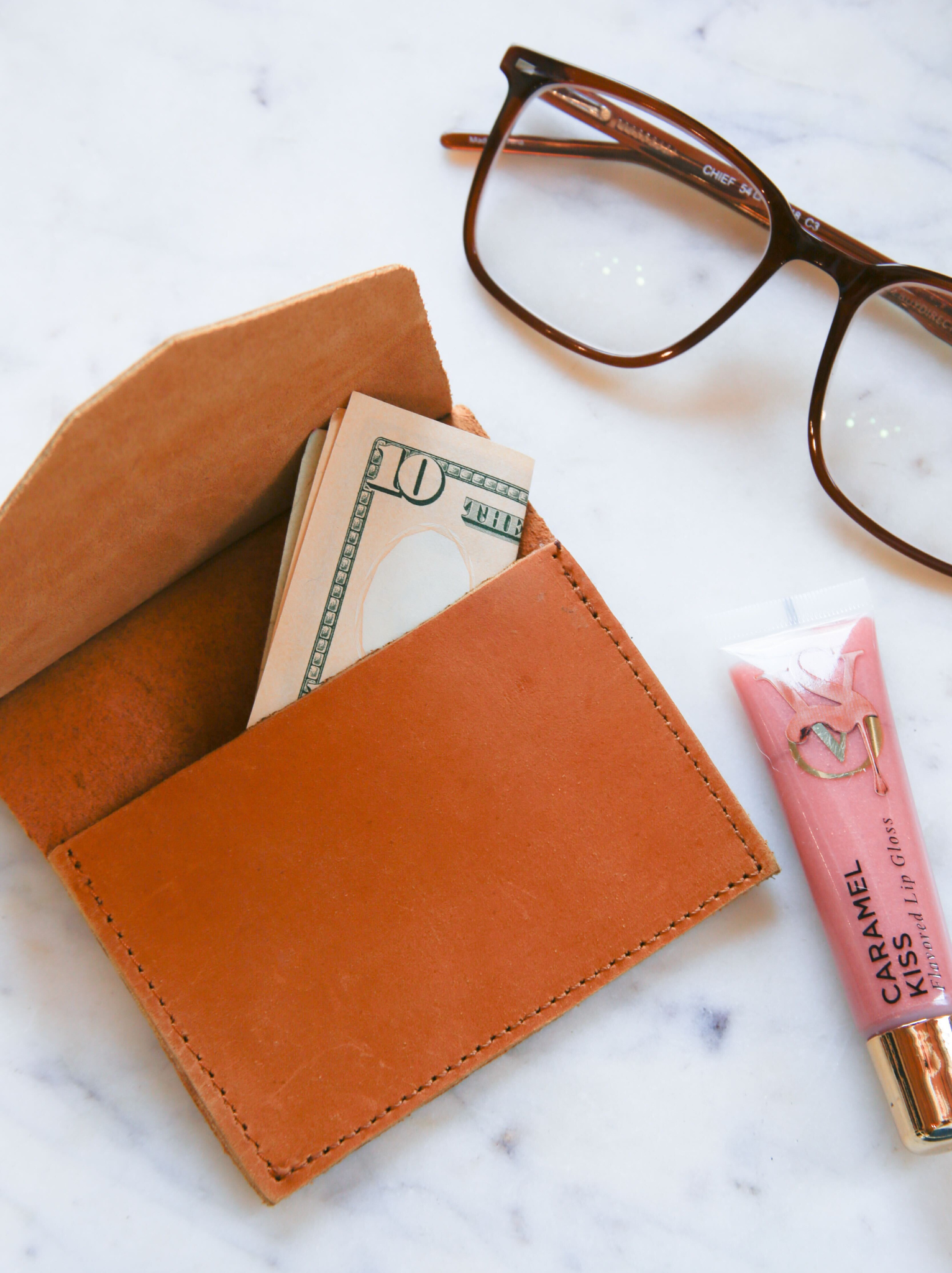 Lita Leather Envelope with money, glasses, and lip balm on a marble surface