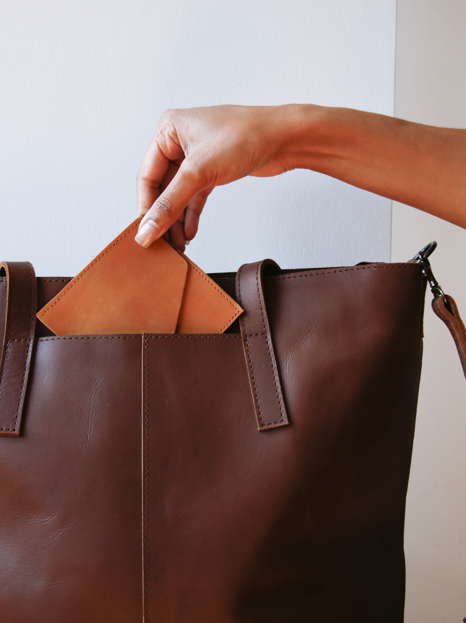 Hand holding a Lita Leather Envelope putting it into exterior pocket of a brown leather tote bag.