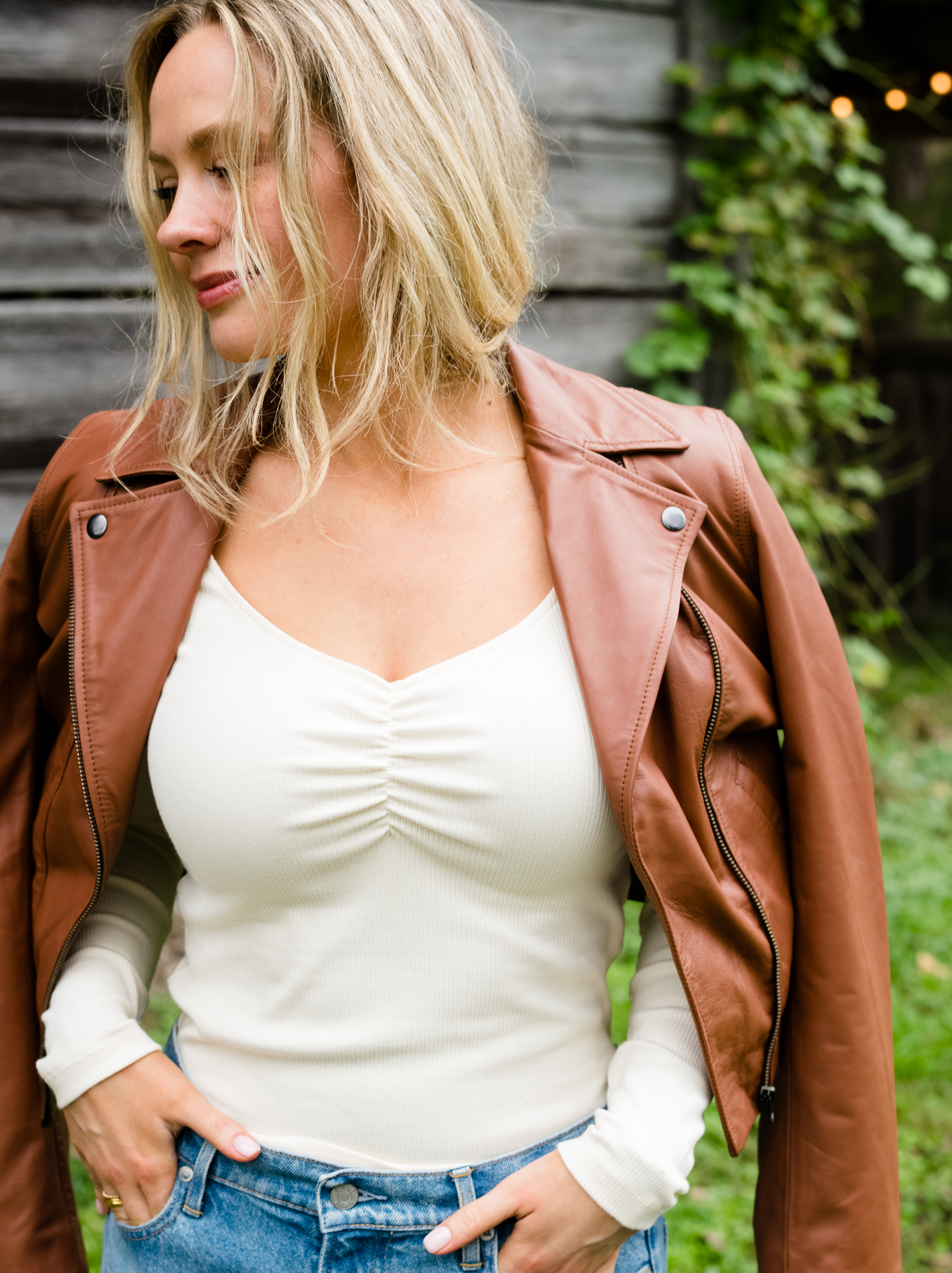 A woman with her hands in her jeans pockets and wearing a Maha Leather Jacket Whiskey