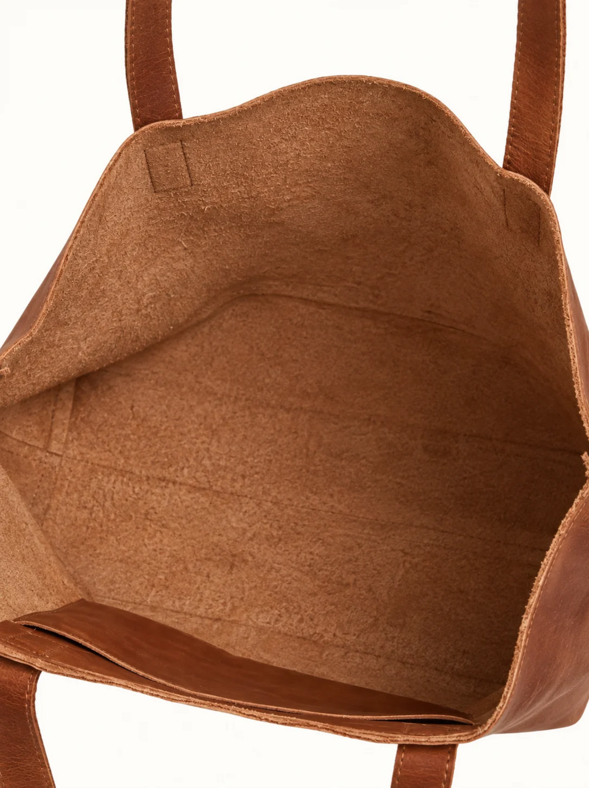 Close-up of the interior of a brown leather tote bag, showing the tan-brown suede  and the brown leather handles against a white background. #Color_Camel