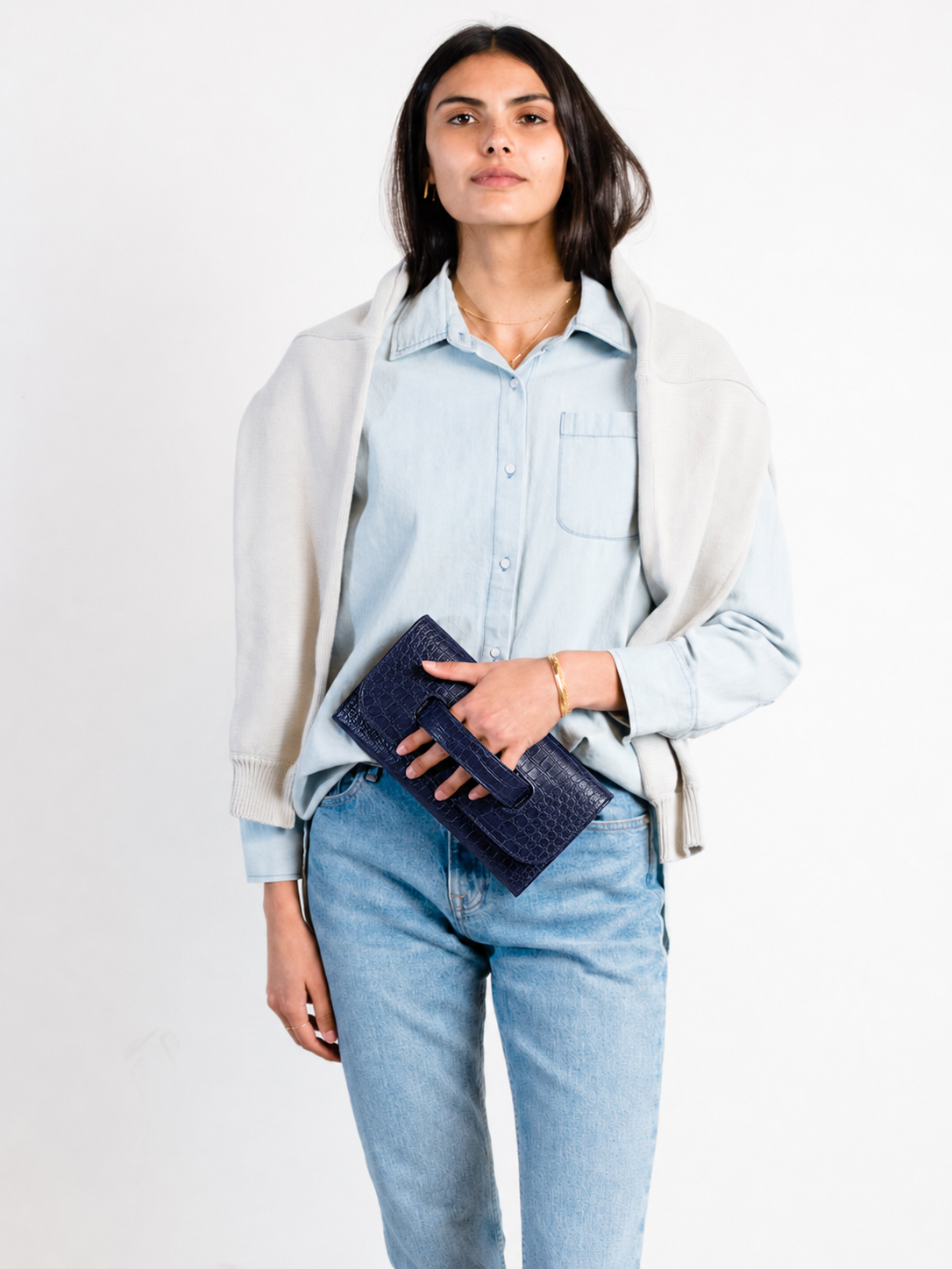 Woman holding a denim outfit holding a blue croc embossed clutch. #Color_Navy Crocodile