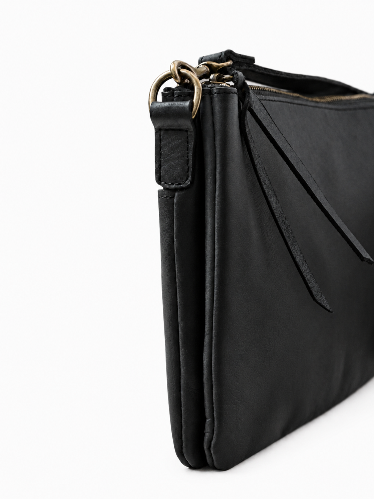 A close-up side view of a black leather crossbody handbag with a bronze-tone metal ring detail and zipper, shown on a plain white background. #Color_Black
