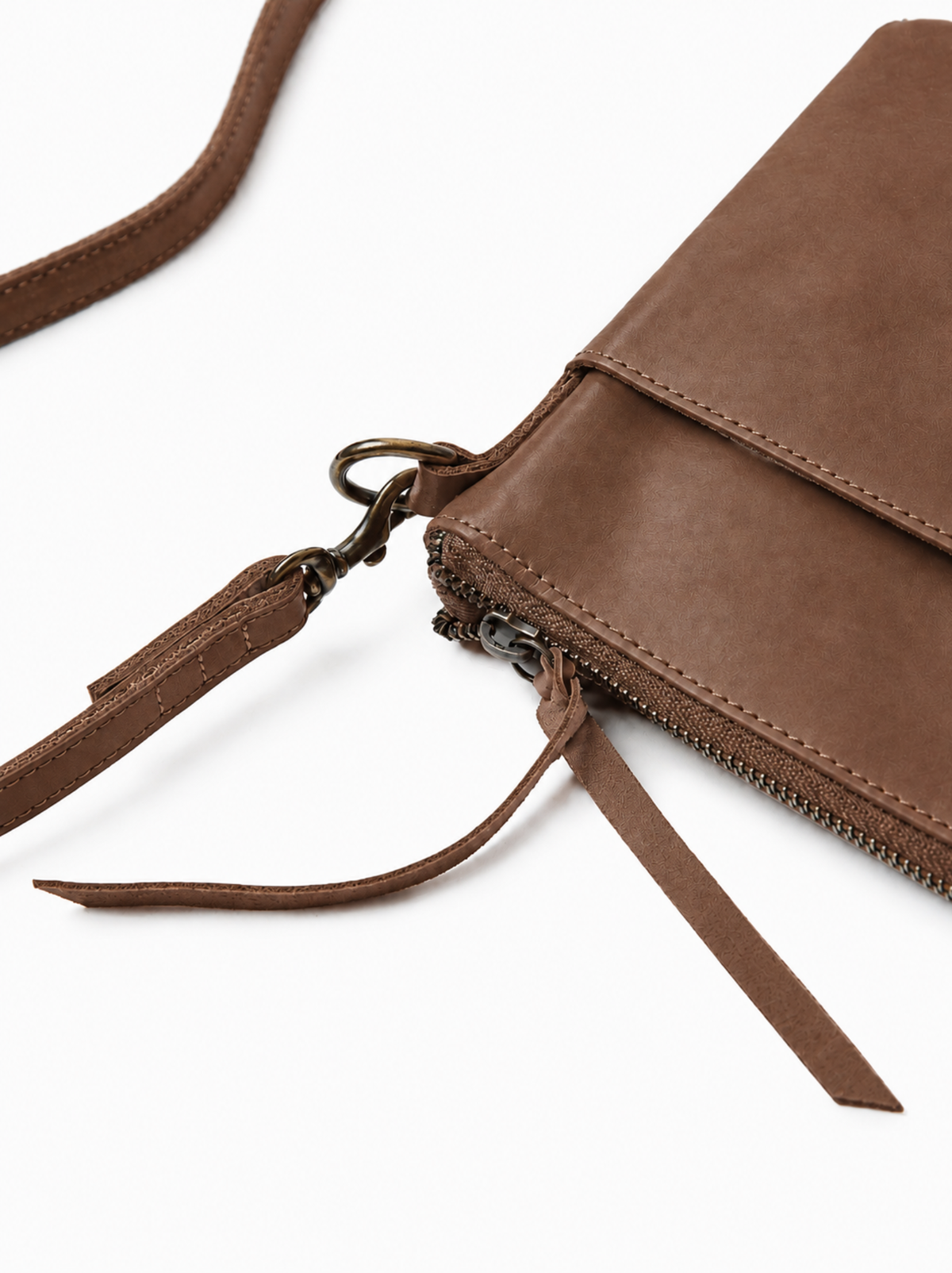 A close-up of a brown leather crossbody bag with a zippered top, showing the texture of the material, metal hardware, and the strap on a white background. #Color_Whiskey