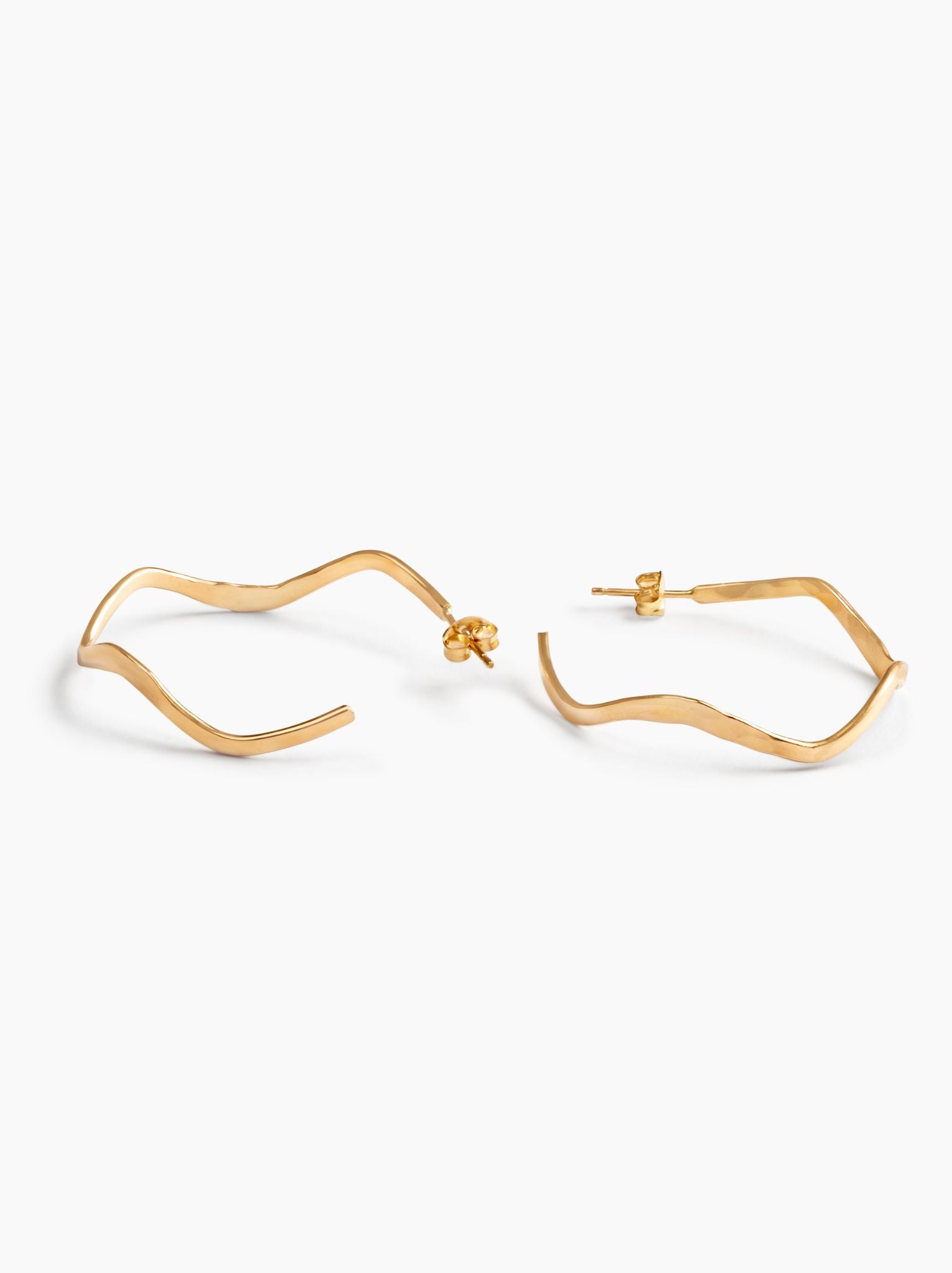 Gold wavy hoop earrings with ear posts lying on their sides on a white background.