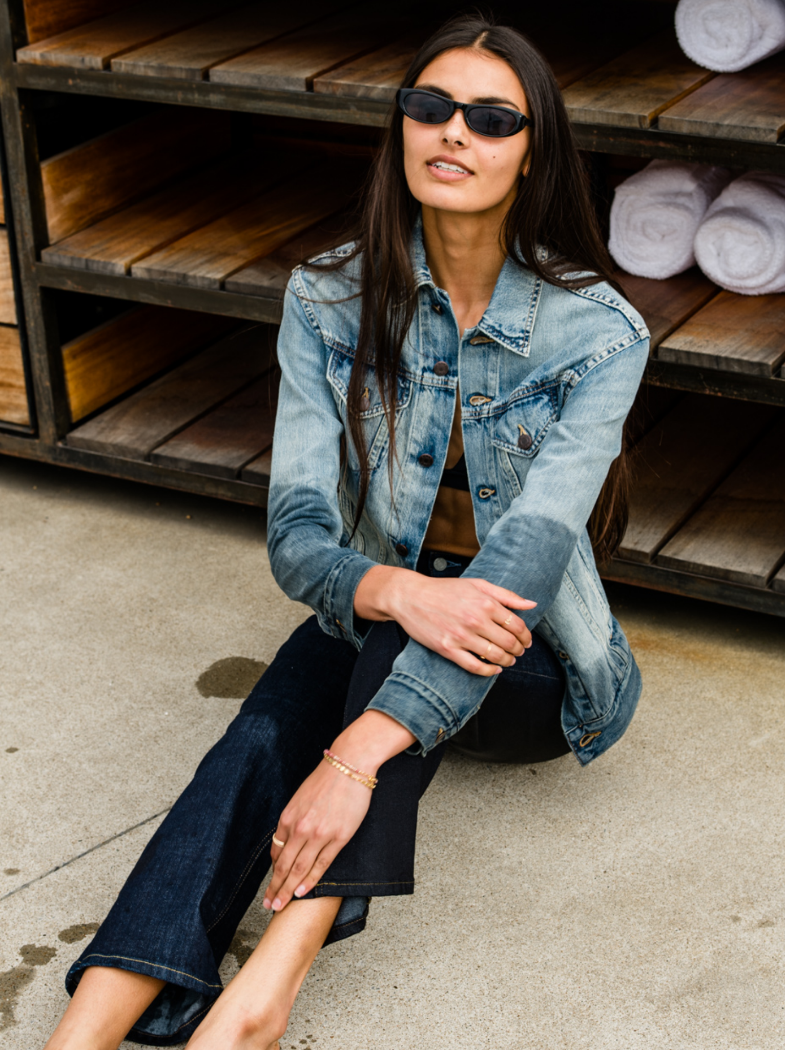 Woman wearing The Merly Jacket sitting on the ground with wooden shelves in the background