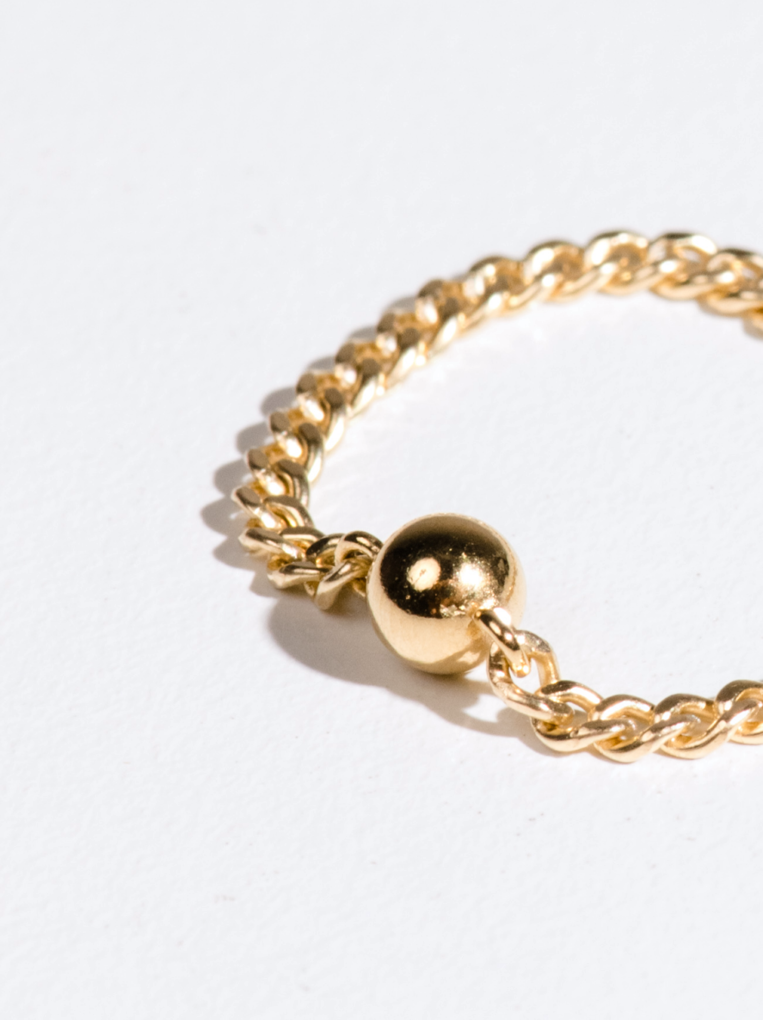 A close up of a gold chain ring with a ball bead accent on a white background.