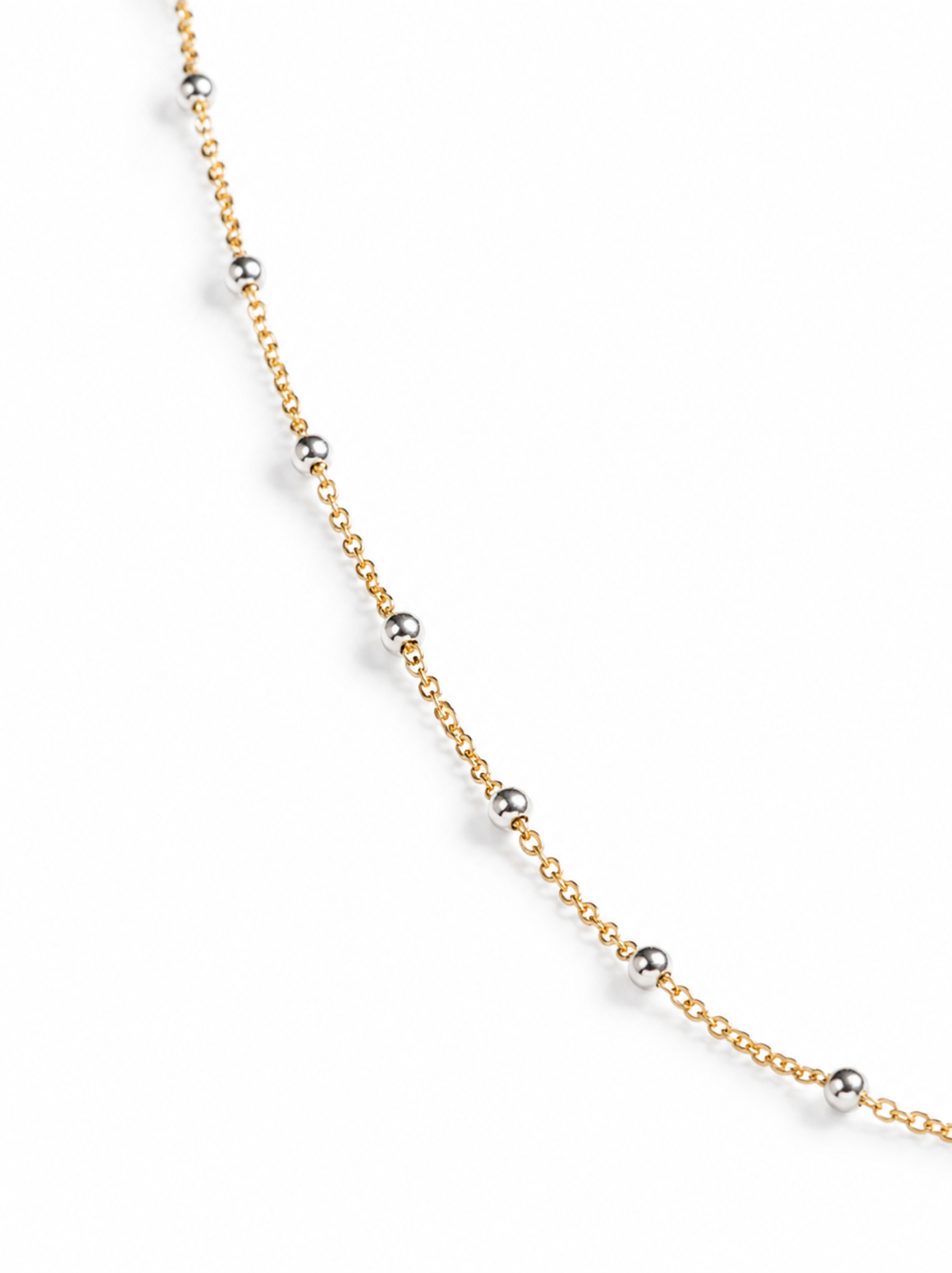 Close up of gold chain and silver beads on a white background.