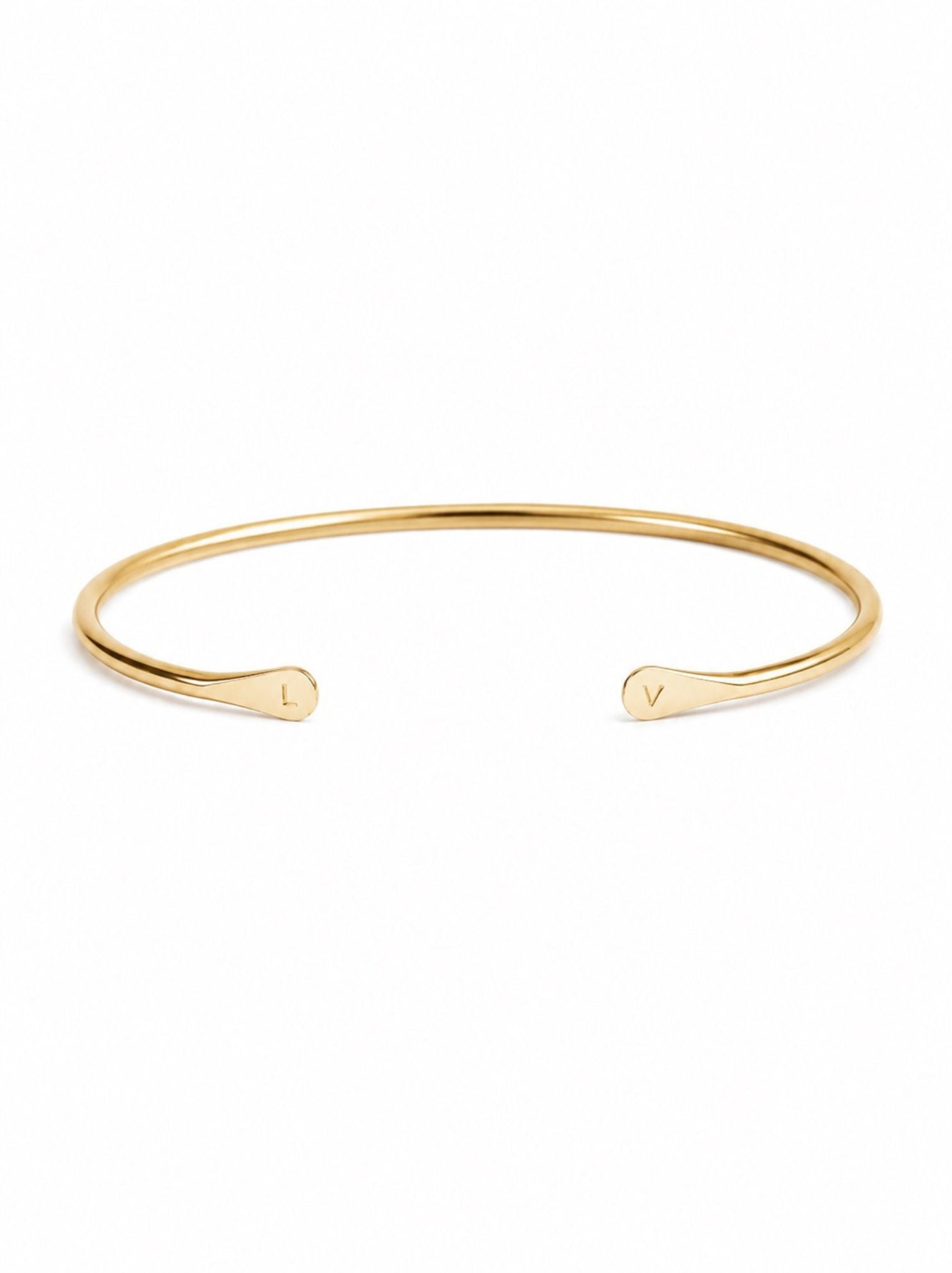 Gold cuff bracelet with front opening featuring a two flattened fronts with a personalized leather on each side on a white background.